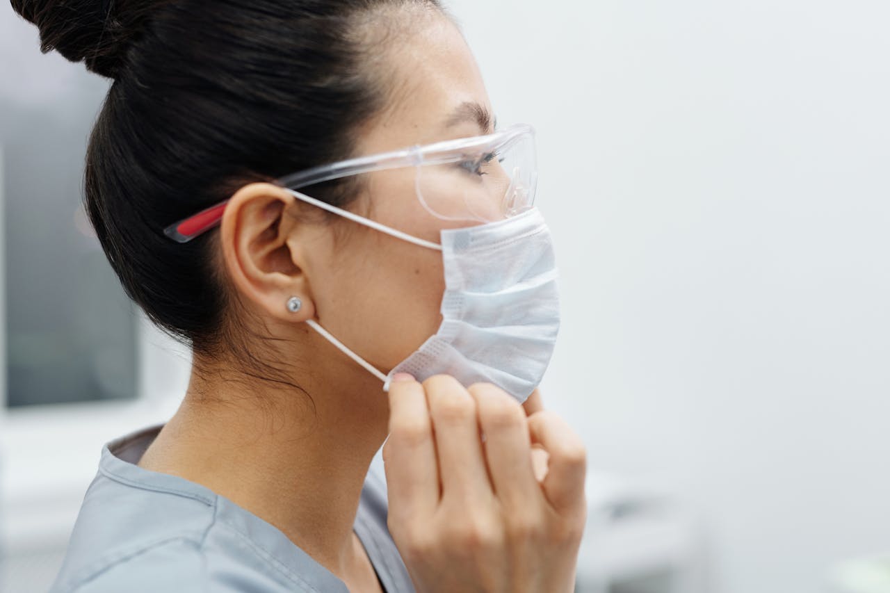Asian female healthcare worker adjusting her protective mask and goggles indoors.